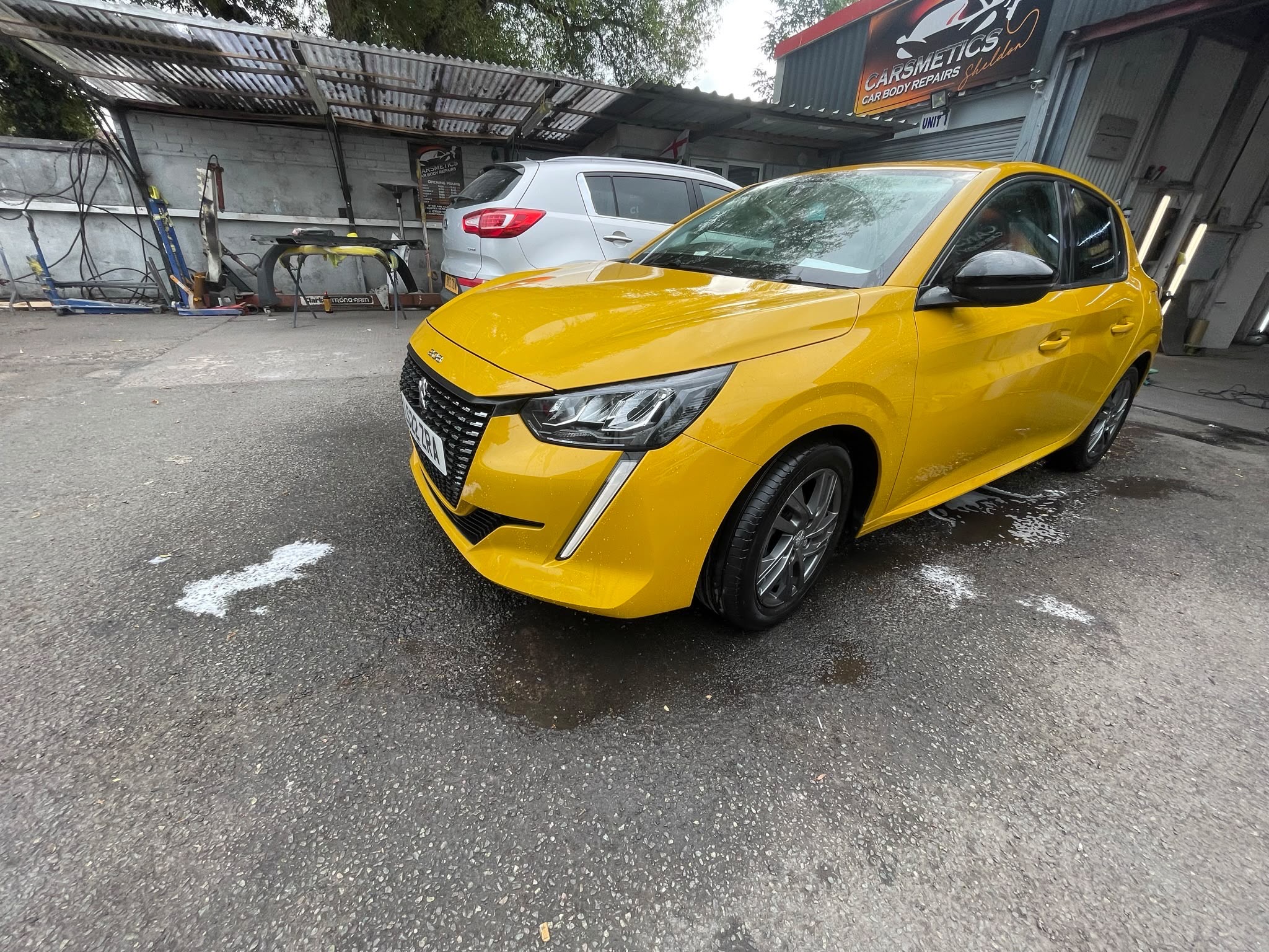 Yellow Peugeot 208 finished outside the workshop